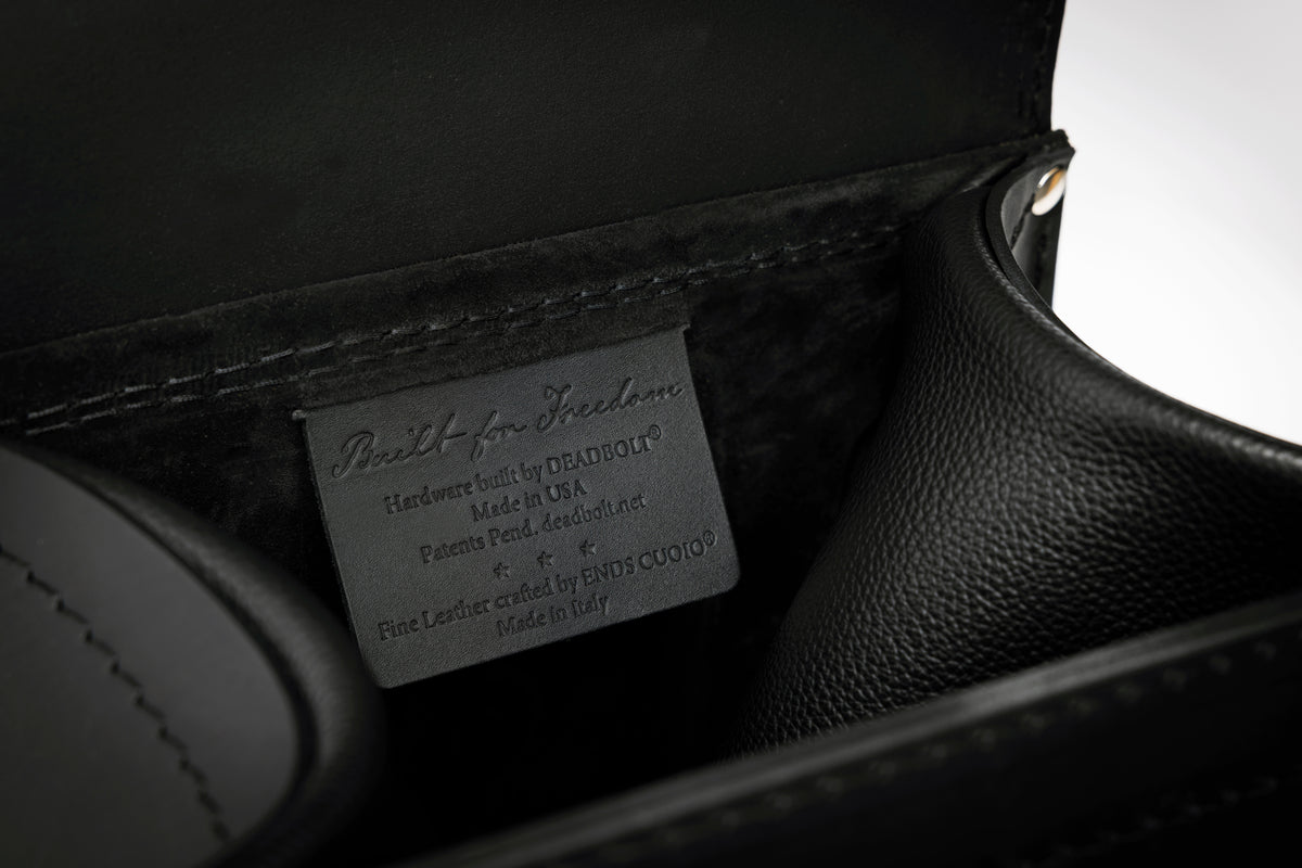 Close-up of the interior of a black leather bag, showing a gray label that reads 'Built for Freedom' and 'Hardworker Made by DEADPOOL'.